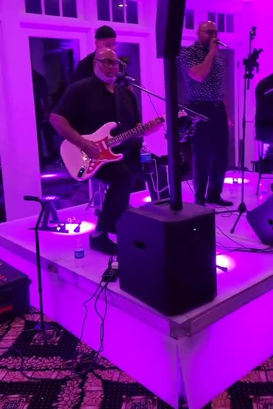 Guitarist performing on a lit stage riser with purple uplighting