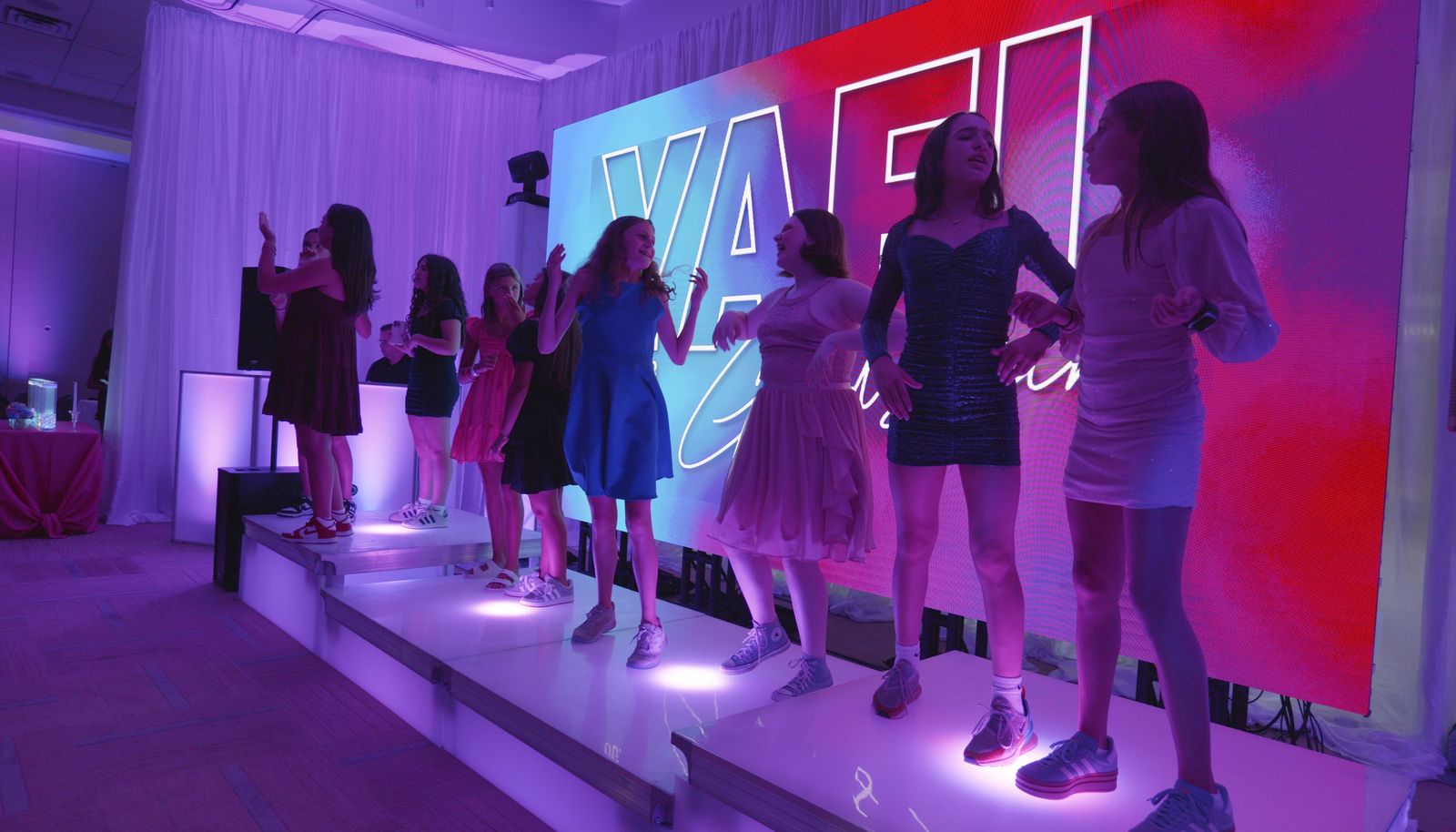 Girls dancing on glowing LED dance boxes in front of a name wall at a Bat Mitzvah