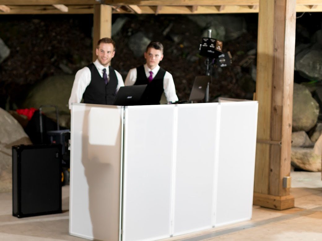 Two ATG DJs behind the clean white facade DJ booth