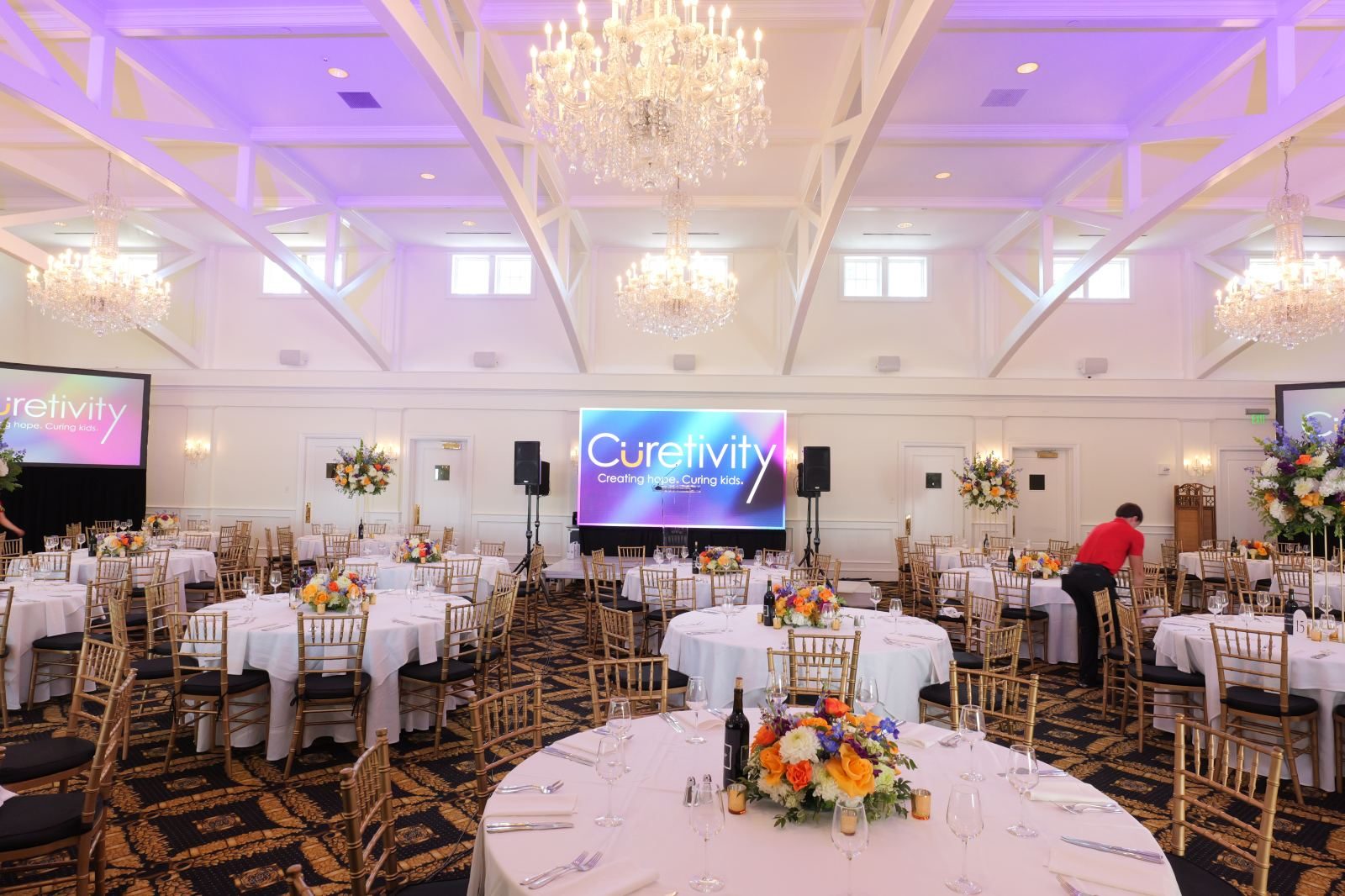 Gala ballroom with purple uplighting, chandeliers and two ATG video screens