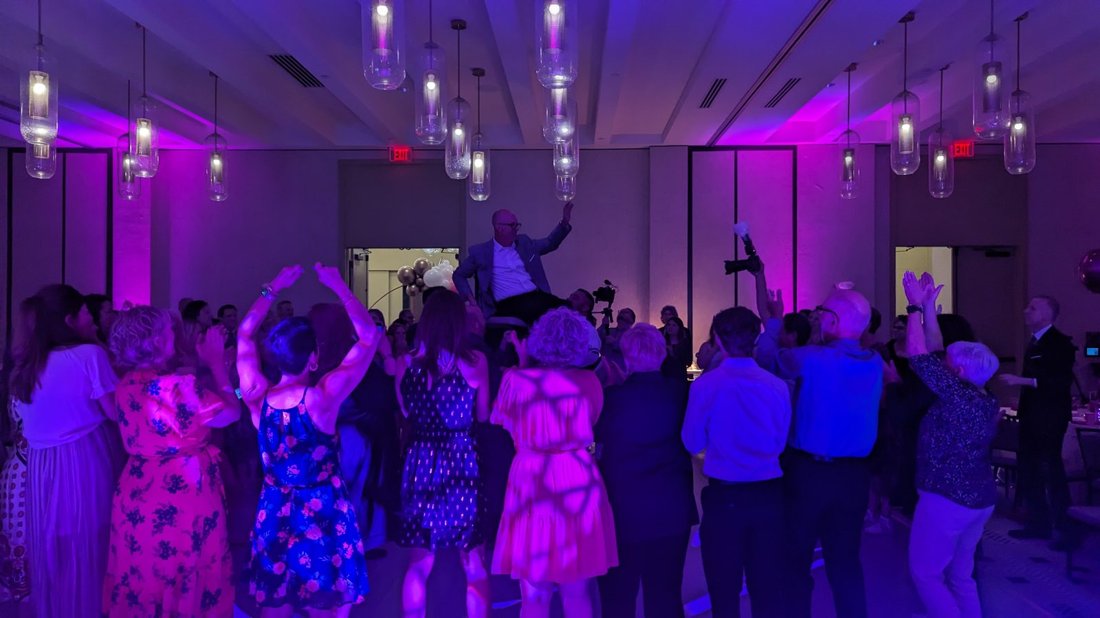 Bat Mitzvah girl lifted in a chair above a dancing crowd in purple light